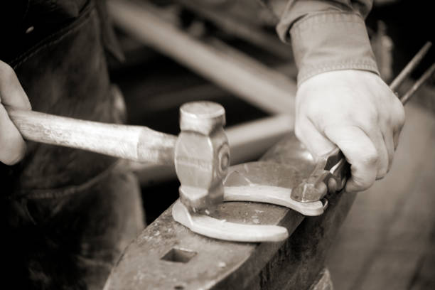 A farrier hammering a red hot horseshoe into shape on his anvil