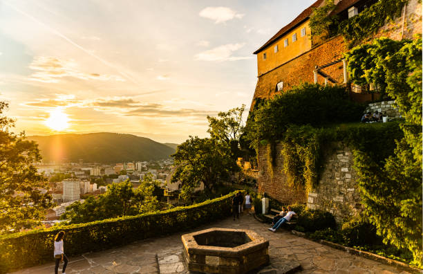vue sur le célèbre château de la colline de schlossberg et souhaite bien. au-dessus de la ville de graz pendant le coucher du soleil en été - graz clock tower clock austria photos et images de collection
