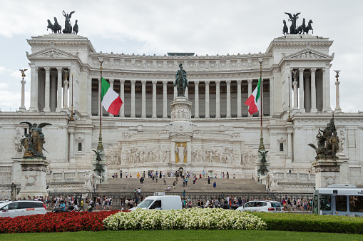 Rome - July 20th 2014: Horizontal view of Italian flags and facade of Vittoriano monument, also known as Altare della Patria, symbol of Italian union, on a cloudy day. Entrance and stairs crowded with tourists.