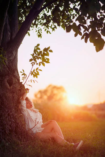 istock Young woman sitting under a tree in sunset 1169803494