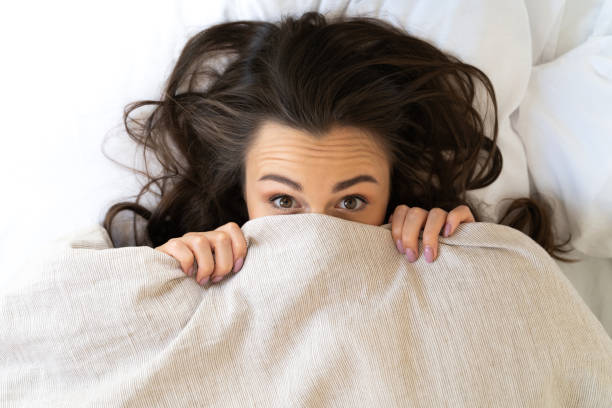 istock Cute young woman hiding face under blanket 1169804587