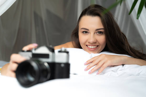 istock Joyful young woman lying in bed and holding retro camera 1169804752