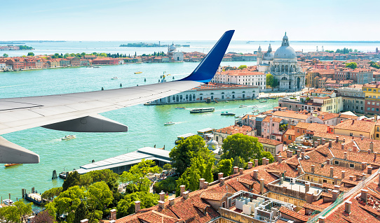 Plane flies above Venice, Italy. Aerial panoramic view of city and sea from airplane window. The plane's wing over Venice during taking off or landing. Concept of flight, vacation and summer travel.