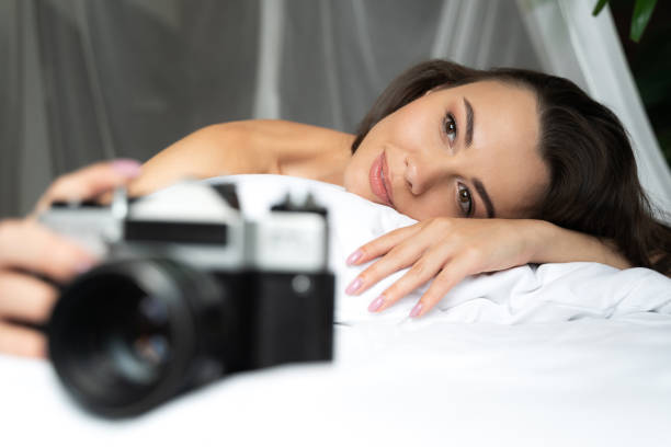 Charming young woman lying in bed and holding retro camera