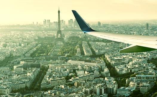 Plane flies above Paris, France. Aerial panoramic view of Eiffel tower from airplane window. The plane's wing over streets of Paris. Concept of air travel to Paris. Flight in Europe in summer.