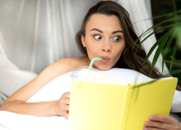 Amazed young woman reading book and drinking cocktail