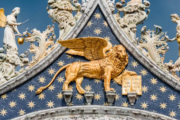 Photo of Golden winged lion with parchment as roof decoration of Basilica San Marco in Venice, Italy, summer time