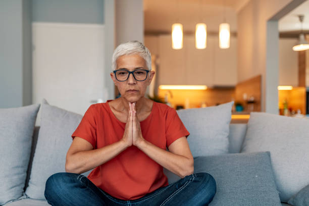 istock Calm senior woman practicing yoga meditating on couch 1169813096