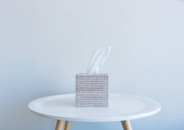 Tissue box on small white table against wall Close up of white tissue in rattan box on small table against neutral wall background - grief concept facial tissue stock pictures, royalty-free photos & images