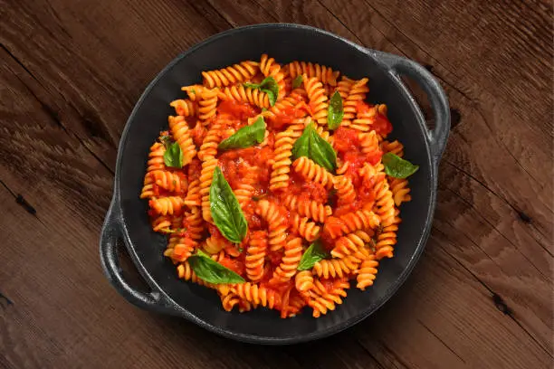 Fresh Italian Pasta served on rustic black pan. Isolated on wooden background.