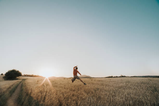 istock Young boy jumping in a wheat field at sunset next to the sun's rays 1169834889