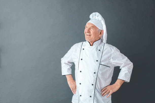 istock Senior chef studio standing isolated on gray hands on hips looking aside dreamful 1169834959