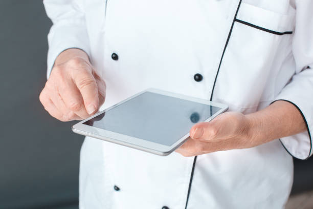 istock Senior chef studio standing isolated on gray tocuhing screen on digital tablet close-up 1169835231