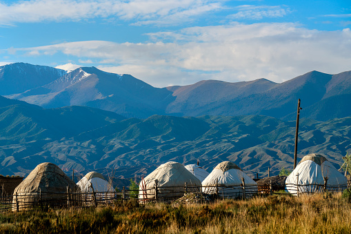 Photo of group of traditional yurts in Kyrgyzstan.  There is no people. Yurts are in a row. The sky is cloudy.