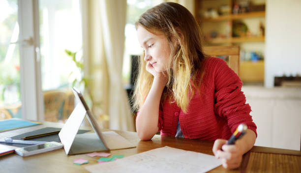 Smart preteen schoolgirl doing her homework with digital tablet at home. Child using gadgets to study. Smart preteen schoolgirl doing her homework with digital tablet at home. Child using gadgets to study. Education and learning for kids. lithuania photos stock pictures, royalty-free photos & images