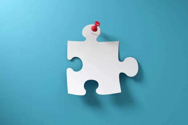A puzzle piece with red thumbtack pinned to blue paper background.