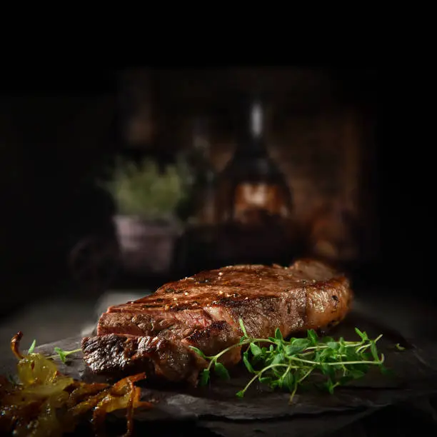 Succulent Farmhouse Rustic Rump Steak with thyme garnish shot against a dark background with wood burner. The perfect image for your bistro or restaurant menu cover art. Copy space.