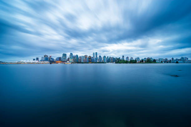 An early morning view of Vancouver, BC , with English Bay in the foreground and a cloudy sky as the sun rises.