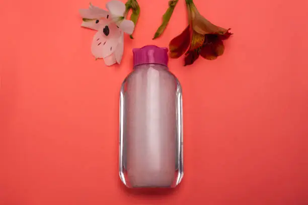Skincare cosmetic bottle with flowers, product for cleansing,make-up remove, top view.Facial tonic, miccelar water, skincare. Mock-up for branding,copy space,pastel color background,minimalistic style