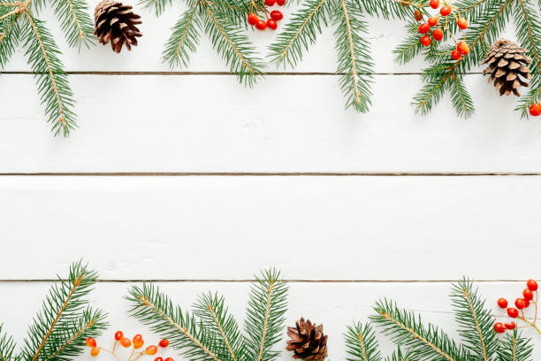 istock Christmas frame made of fir tree branches, red berries, pine cones on rustic wooden white background. Christmas, New Year, winter holidays concept. Flat lay, top view, copy space 1169887270