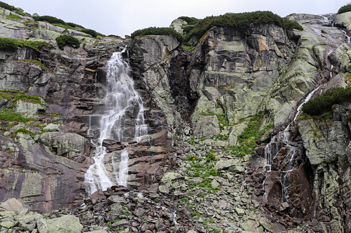 Mountain waterfall in High Tatras (Skok). Tall rocks covered with scrub. Large waterfall on the left, small water on the right.