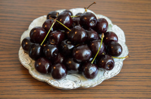 Wet chilled cherries with peduncles on saucer on table