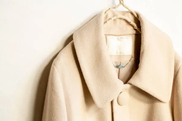 Photo of beige wool coat hanging on clothes hanger on white background