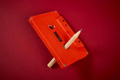 orange audio cassette and pencil on dark red background