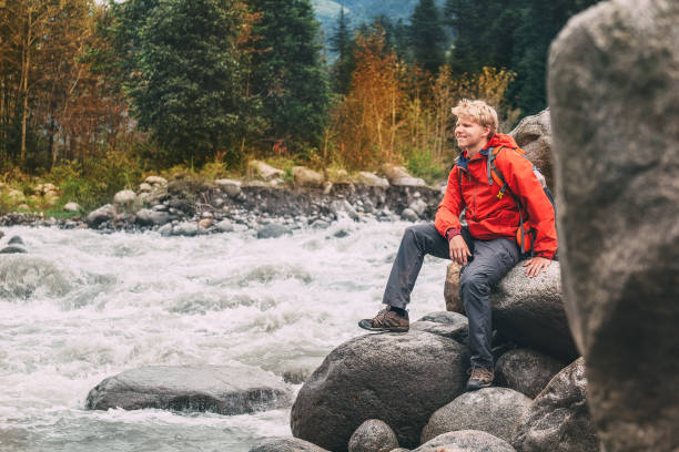 Young man tourist sits  rocky mountain river bank Young man tourist sits  rocky mountain river bank indian boy barefoot stock pictures, royalty-free photos & images