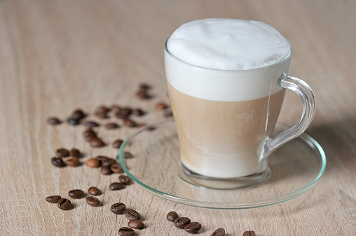 Cappuccino in a transparent cup on a light surface. Coffee beans on the surface of the table. Close-up. The vertical orientation of the frame.