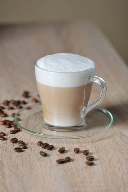 Cappuccino in a transparent cup on a light surface. Coffee beans on the surface of the table.