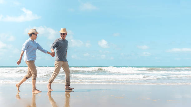 glücklich senior mann und frau paar tanzen, halten hände & spritzen im meerwasser an einem einsamen tropischen strand mit hell klarem blauen himmel - couple senior adult travel action stock-fotos und bilder