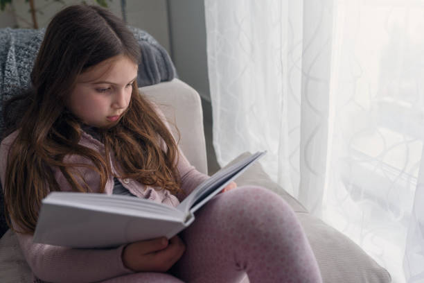 istock Child reading a book, at home by the window. 1169917410