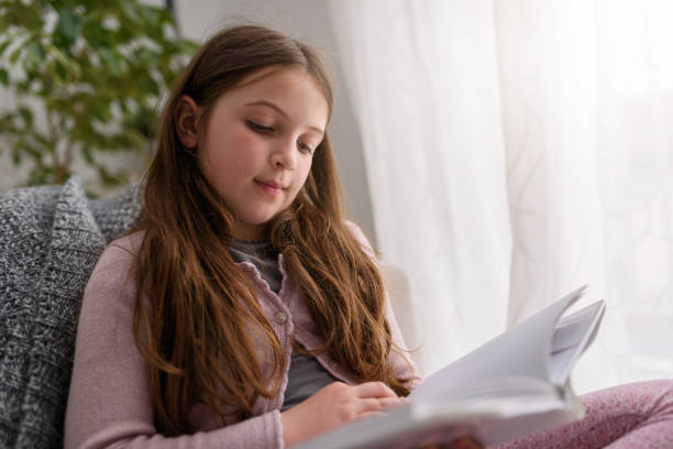 istock Child reading a book, at home by the window. 1169917414