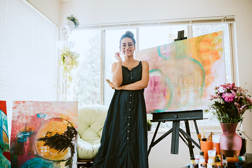 An Indian American woman works on large painted art canvases in the comfort of her apartment living room.