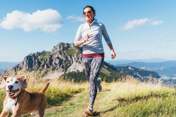 istock Happy smiling female jogging by the mounting range path with her beagle dog. Canicross running healthy lifestyle concept image. 1169926425