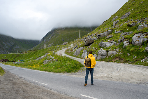 Man in yellow hoodie and backpack chooses the road. Simple or difficult road. Way through the city or into mountains. Wanderlust. Leisure activity, hiking. Adventure lifestyle. Explore North, Norway