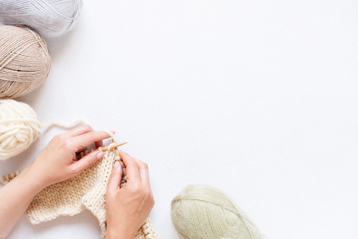 White background with knitting and female hands, balls of various pastel yarn and knitting process on the white table, copy space