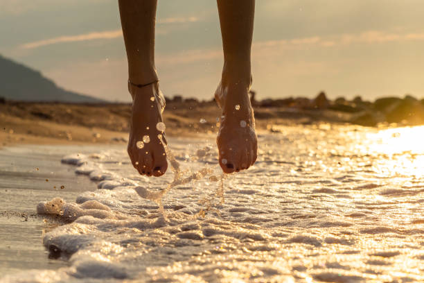 Feet of a girl walkin over the sea water at dawn stock photo