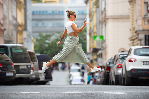 Blonde cool woman crossing street, jumping, hovering, checking phone