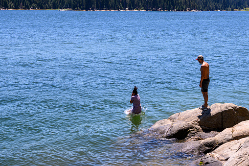 One young female Latino adult jumping off the rocky shore, of remote mountain lake, with male Latino adult waiting for his turn.

Taken at Shaver Lake, California, USA