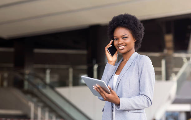 istock Young woman talking on cellphone, using digital tablet near modern office building 1169956337