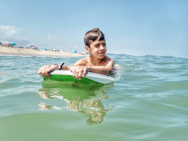десятилетний мальчик плавает на доске для серфинга в саут-бетани-бич делавэр - skimboard стоковые фото и изображения