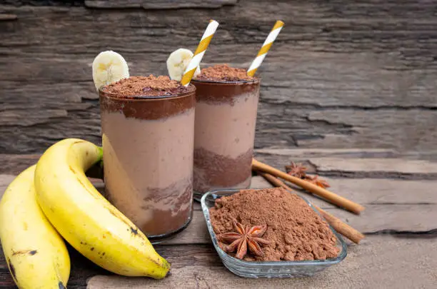 Photo of Banana blended chocolate yogurt smoothies milk high protein drinks brown put a glass on a wooden background.