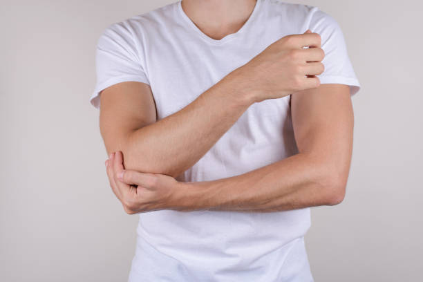 Cropped close up photo portrait of unhappy upset sad guy holding touching painful elbow wearing white t-shirt isolated grey background copy space Cropped close up photo portrait of unhappy upset sad guy holding touching painful elbow wearing white t-shirt isolated grey background copy space forearm stock pictures, royalty-free photos & images