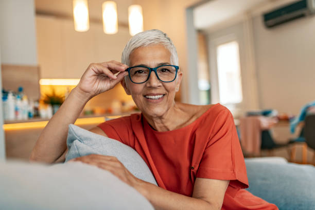 There is no other way I would want to spend my weekend Happy mature woman relaxing on her couch at home in the living room. Close up face of senior woman looking at camera. Portrait of happy woman in red shirt smiling while holding eyeglasses. Happy woman relaxing on her couch at home in the sitting room. Smiling senior woman sitting in couch at home one mature woman only stock pictures, royalty-free photos & images