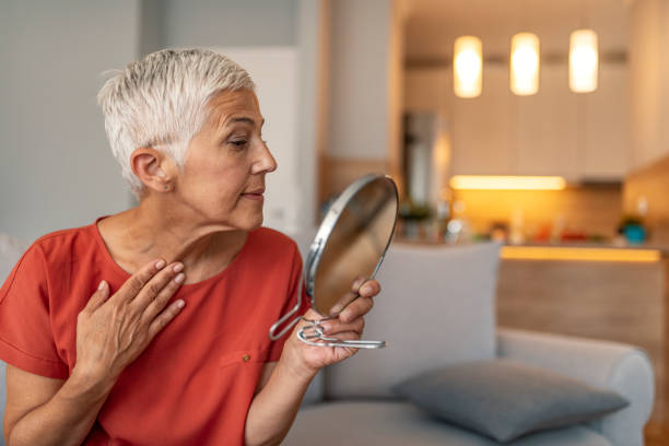 mujer madura con espejo de maquillaje masajeando su cara y cuello - wrinkled women mature adult beauty fotografías e imágenes de stock