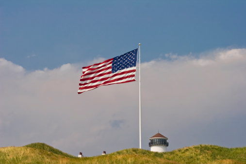 American Flag with Top of Lighthouse, Dunes and Stormy Sky