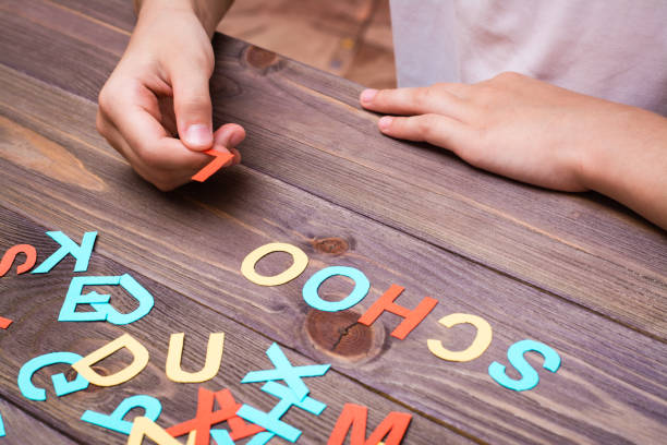 le mani dei bambini compongono la parola "scuola" da lettere di cartone intagliato colorate - child alphabetical order writing alphabet foto e immagini stock