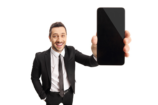 Young man in a suit and tie holding a mobilephone in front of the camera isolated on white background